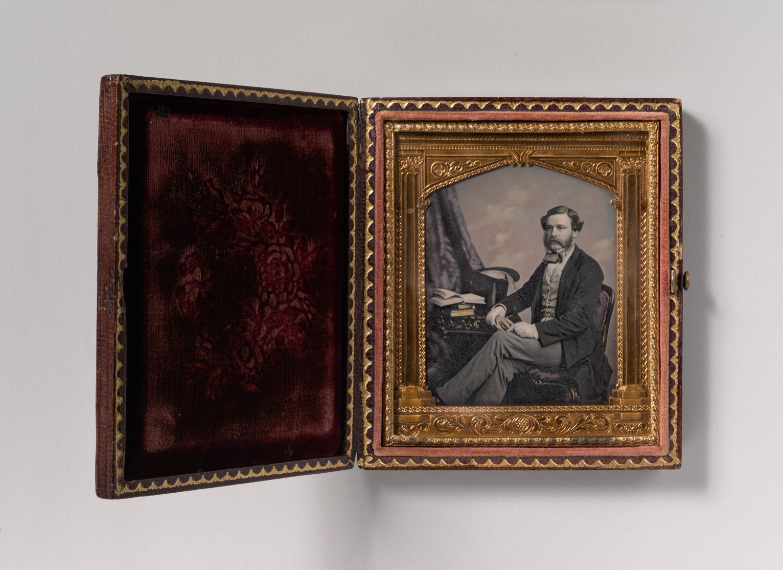 [Man Seated in Front of Cloud Backdrop, Books and Top Hat on Table] — Unknown