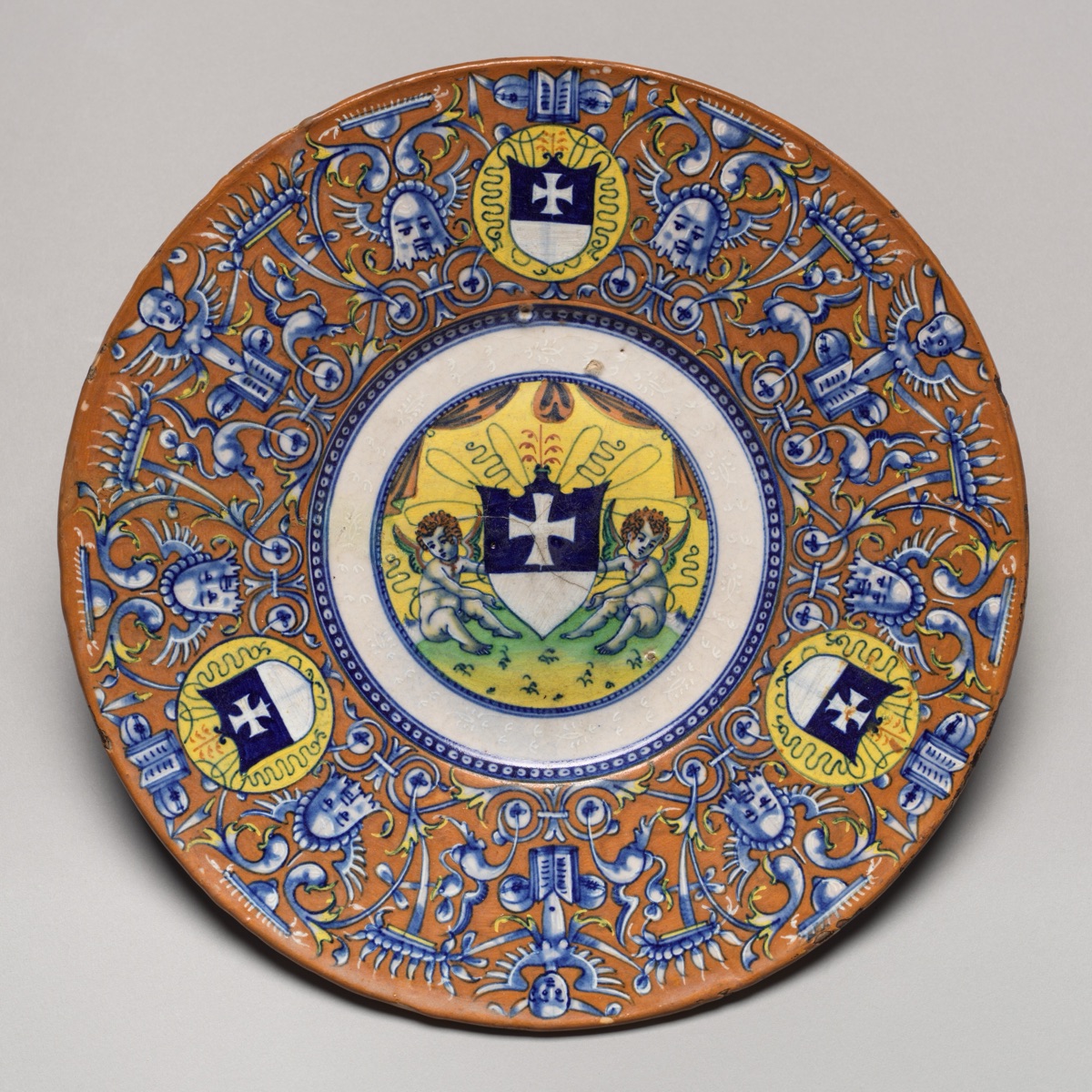 Plate with border of grotesques on an orange ground and three shields of the arms of the Gritti of Venice; in the center, putti holding another shield of the same arms — Venetian 16th Century; Faenza 16th Century; Probably Faenza or Venice 16th Century