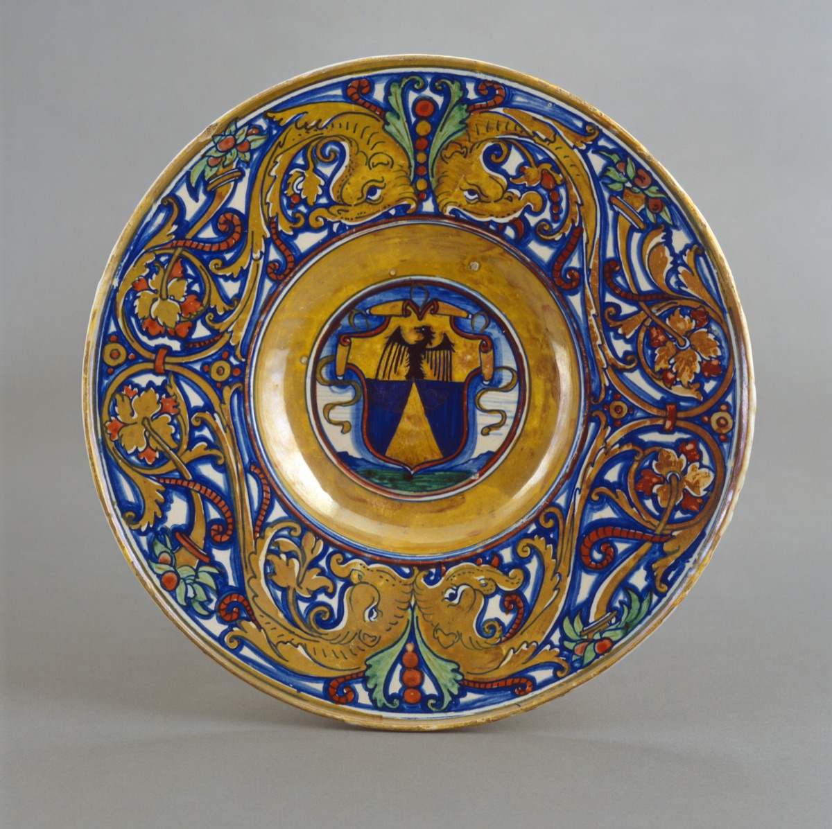 Plate with border of foliate scrollwork with dolphin heads and cornucopias; in the center, shield of arms of Vigerio of Savona — related artist: Maestro Giorgio Andreoli of Gubbio; Italian 16th Century; Workshop of Maestro Giorgio Andreoli of Gubbio